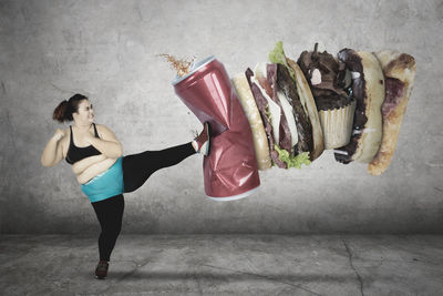 Digital composite image of woman kicking fast food against wall