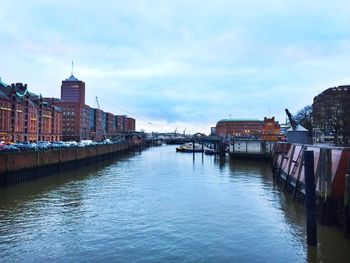 Bridge over river by buildings in city against sky