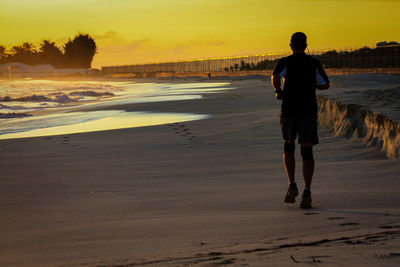 Rear view of man walking on beach during sunset