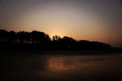 Silhouette trees on beach against sky at sunset