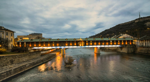 Bridge over a river by buildings against sky during the rainy season