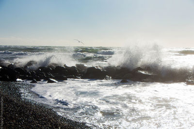 Sea waves splashing on rocks against sky
