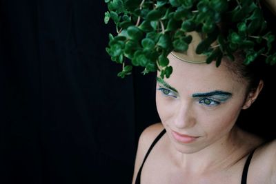 Close-up of thoughtful woman wearing leaves against black background