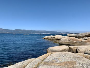 Rocks by sea against clear blue sky