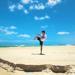 Full length of man exercising on beach against sky