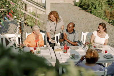 Young female nurse serving food to senior men and women sitting at dining table