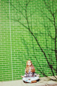 Portrait of smiling young woman sitting against wall