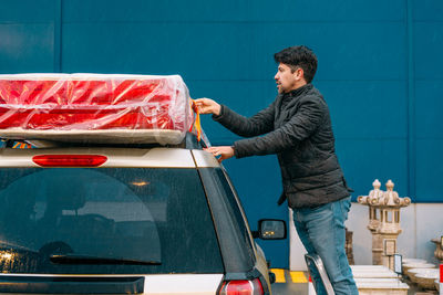 Man securing mattress on car top in a rainy evening