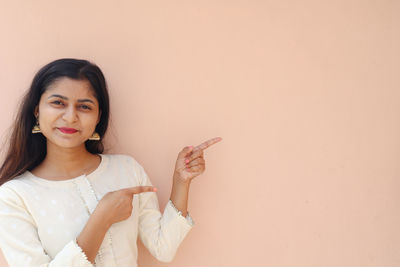 Portrait of a smiling young woman standing against wall