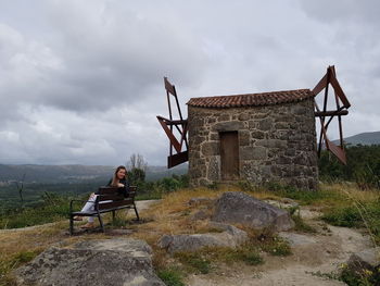 Woman sitting on rock by building against sky