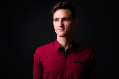 Portrait of young man standing against black background