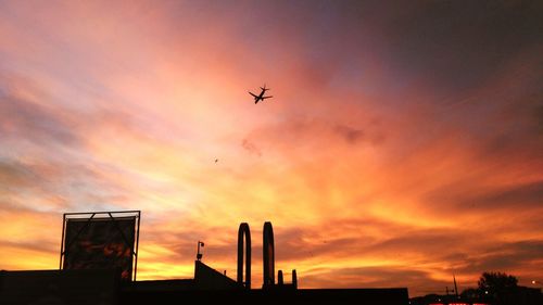 Airplane flying over city against sky during sunset