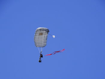 Low angle view of people paragliding against clear blue sky