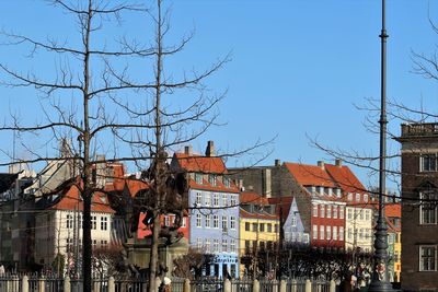 Copenhagen, nyhavn, collarful houses against blue sky, bare trees in the foreground.