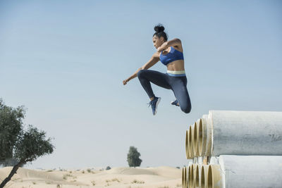 Low angle view of woman jumping against clear sky