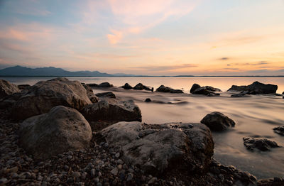 Rocks on shore against sky during sunset