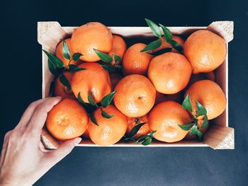 Directly above shot of cropped hand taking orange from wooden crate