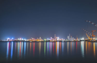 Illuminated city by sea against sky at night