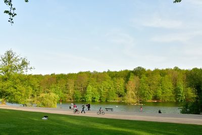 People by lake and trees against sky