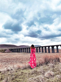 Rear view of woman standing on bridge over field against sky