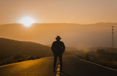 Silhouette of adult man in cowboy hat standing on country road during sunset. almeria, spain