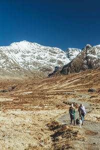 Men walking on snowcapped mountain against clear sky