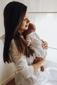 Side view of young woman sitting on bed at home