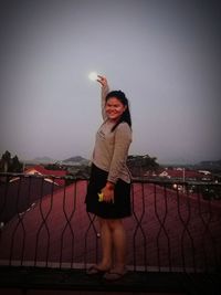 Woman holding umbrella while standing against sky