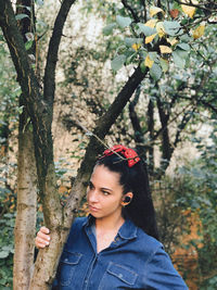 Portrait of young woman standing by tree trunk