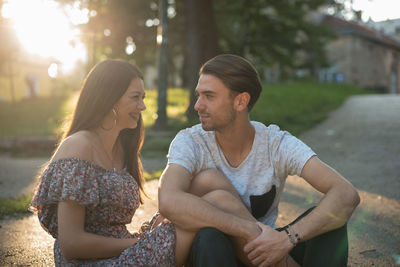 Young couple looking at each other while sitting in park during sunset