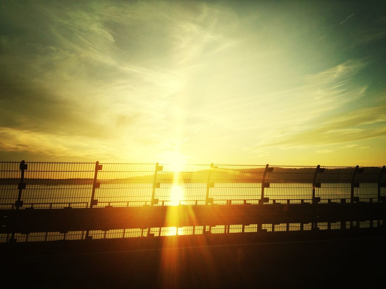 sunset, sun, sky, silhouette, railing, orange color, built structure, sunlight, architecture, bridge - man made structure, sunbeam, cloud - sky, transportation, lens flare, water, nature, connection, beauty in nature, incidental people