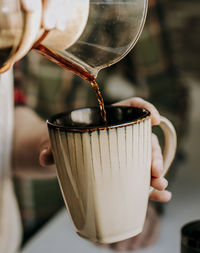 Close up of coffee being poured from pour over into a tan coffee cup