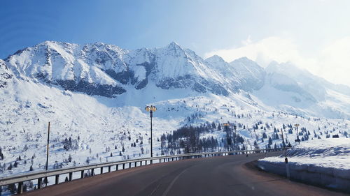 Empty road by snow covered mountains against sky