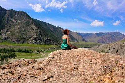 Rear view of young woman sitting on rock against mountains