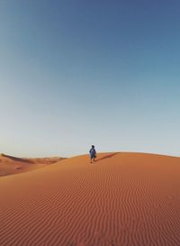 Man on sand dune in desert against clear blue sky