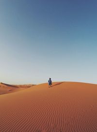 Man walking in desert against clear blue sky