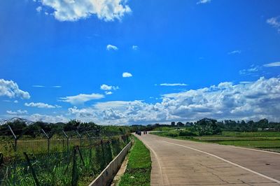 Road amidst field against blue sky