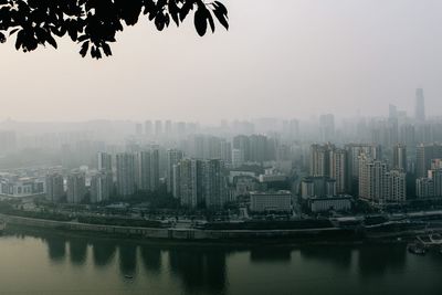 Buildings by river against sky during foggy weather