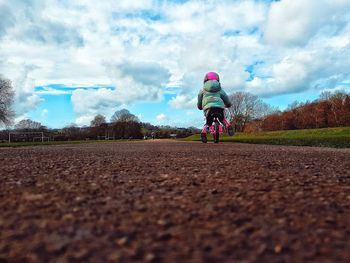 Rear view of boy riding bicycle on road against sky