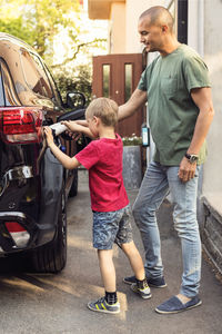 Father and boy charging electric car by house