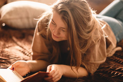 Young happy woman reading book while lying on bed at home