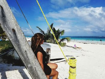 Woman sitting on beach by sea against sky