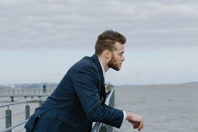 Side view of young man looking at sea against sky