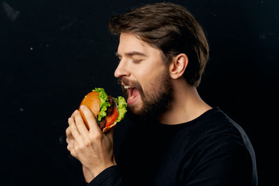 Portrait of young man eating food against black background