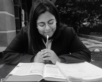 Smiling young woman reading book on desk