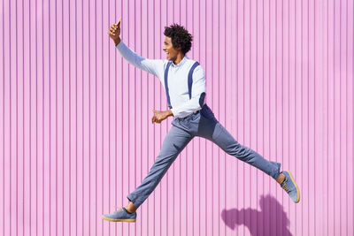 Full length of man with arms raised standing against pink wall