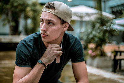 Thoughtful young man wearing cap while sitting outdoors