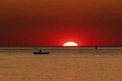 Silhouette boat in sea against orange sky