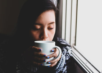  young woman drinking coffee by window