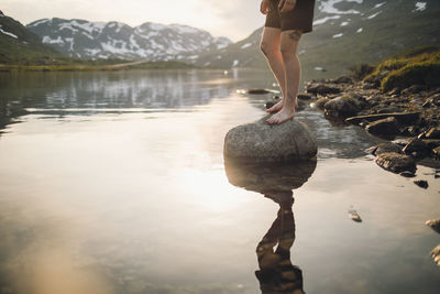 Low section of person standing on rock at lake